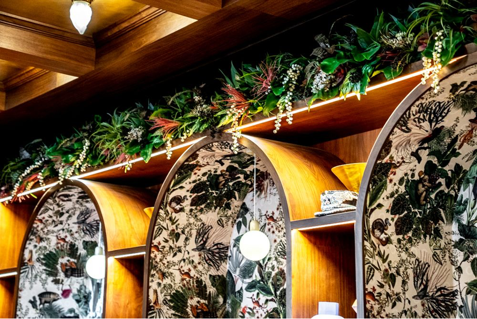 Built in cabinetry with arches at the top, with wallpaper design on the inside of the arches, and greenery hanging above them