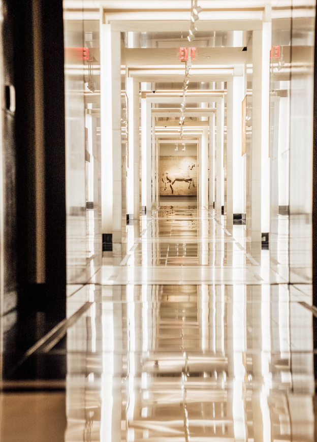 A long, well lit hallway with a big piece of art on the wall at the end