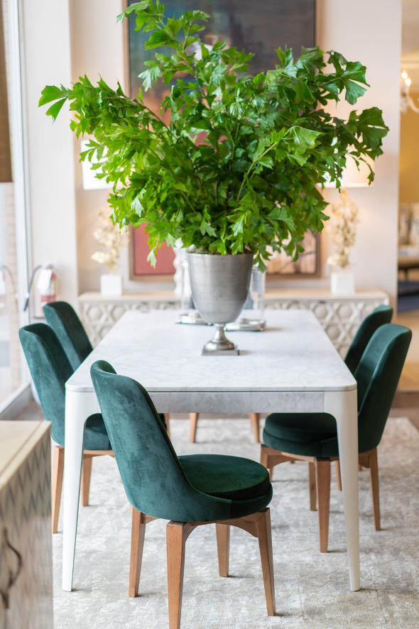 A dining room table with green chairs and large greenery in the center of the table