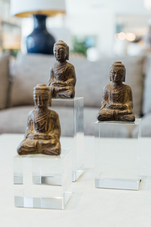Three small, stone buddha statues sitting on glass stands of different heights
