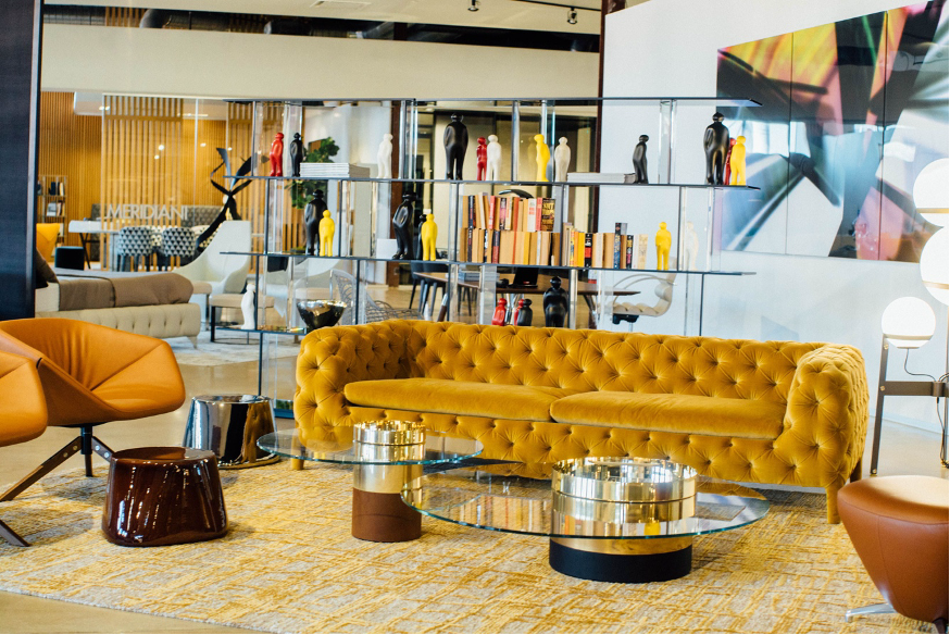 A seating area with a yellow couch, orange chairs, tables, shelves with books and decor, and more