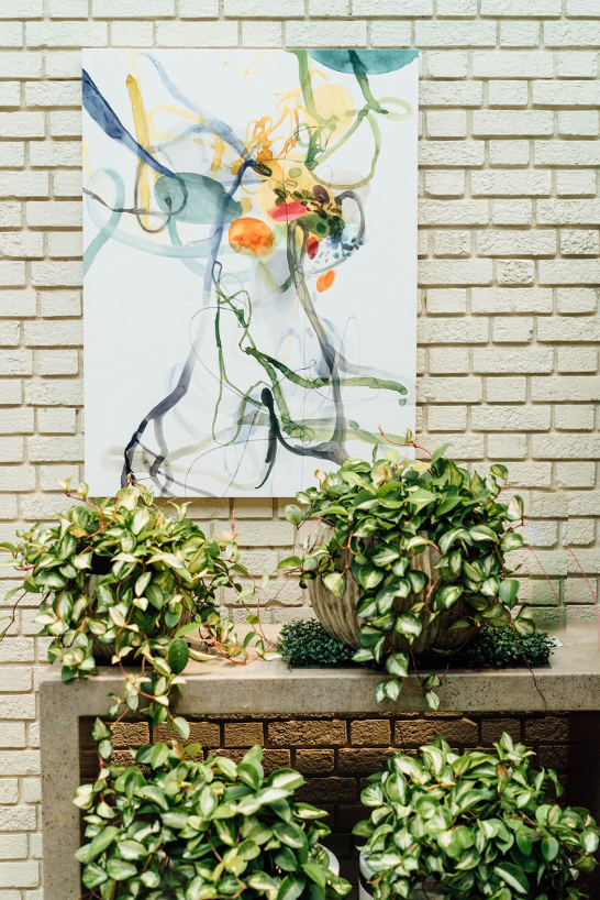 A scene with a piece of art on the wall with a table full of greenery and plants